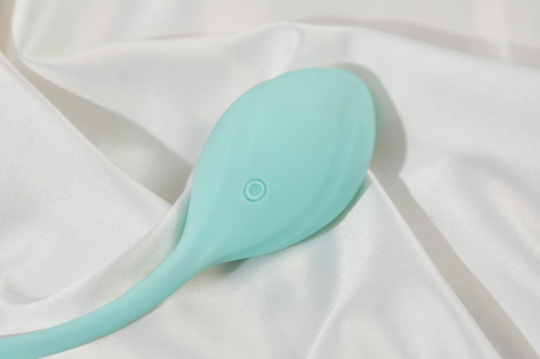 A teal clitoral vibrator on white silk fabric, showing smooth design and texture
