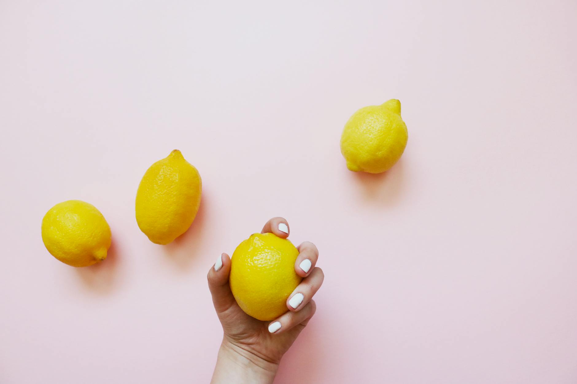 A hand holding a fresh lemon on a soft pink background, symbolizing gentle care and natural wellness.