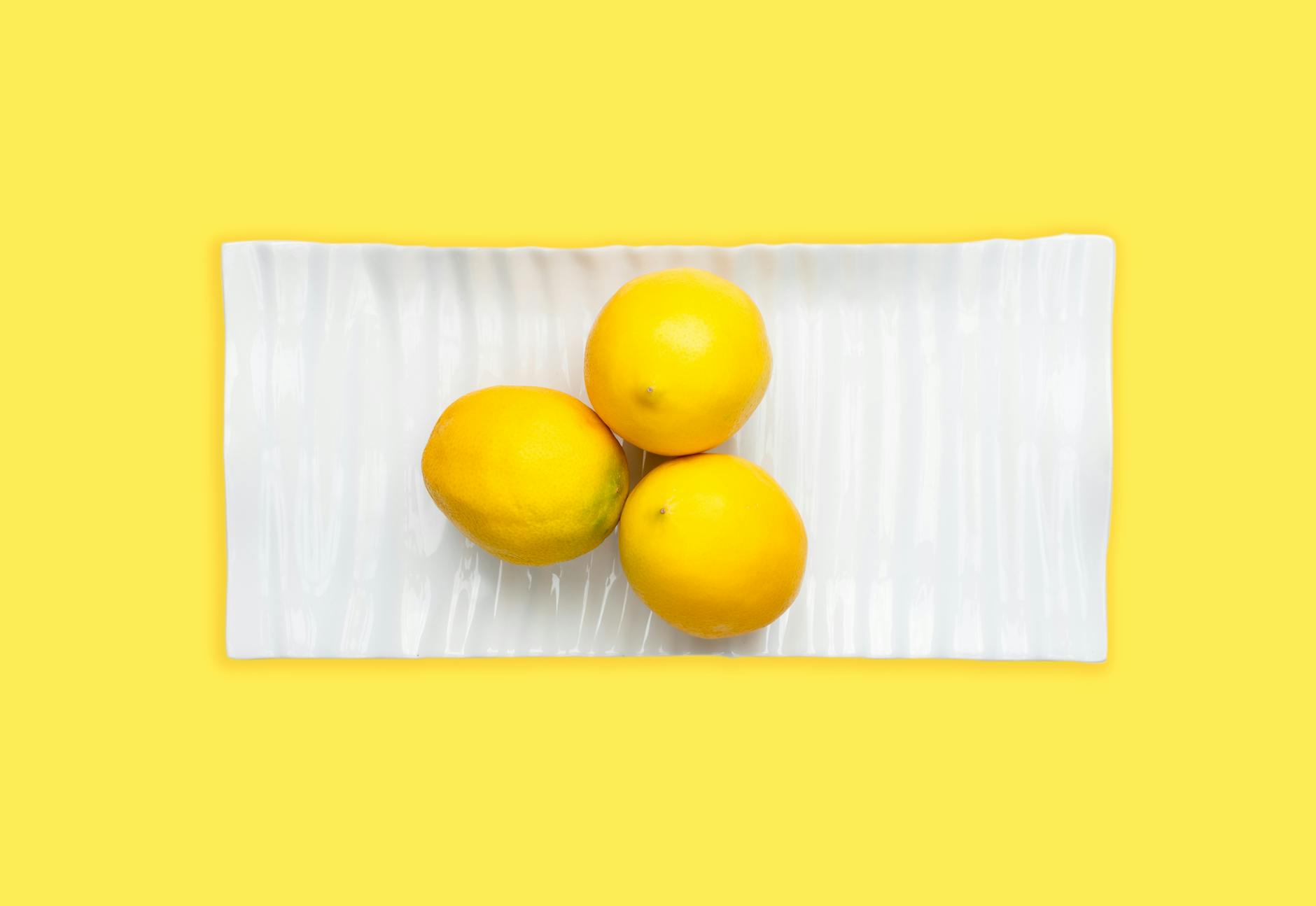 Fresh lemons on white plate with bright yellow background, symbolizing renewal and gentle restoration