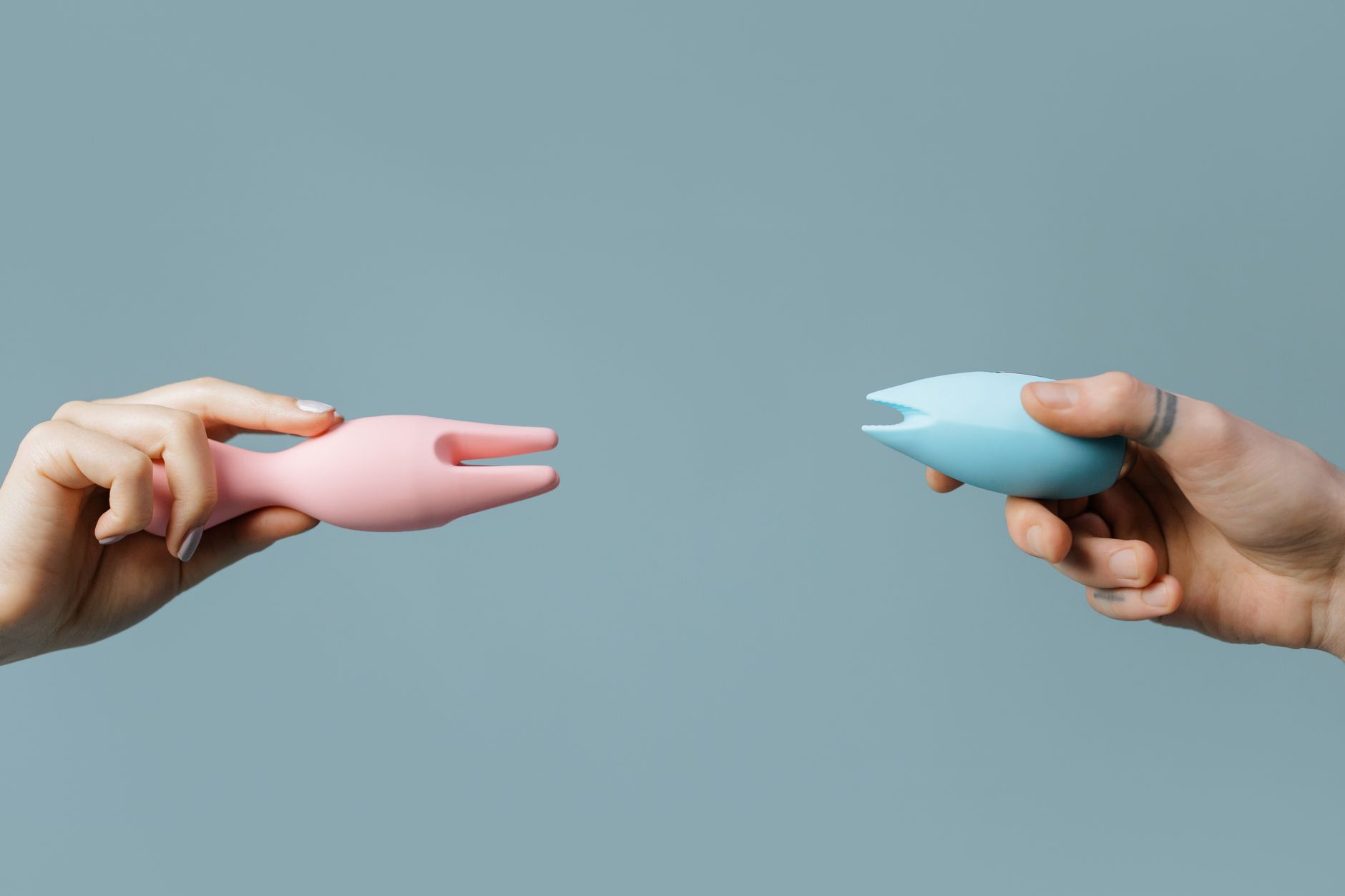 Two hands holding pastel-colored vibrators against a soft background, illustrating intimate couples play