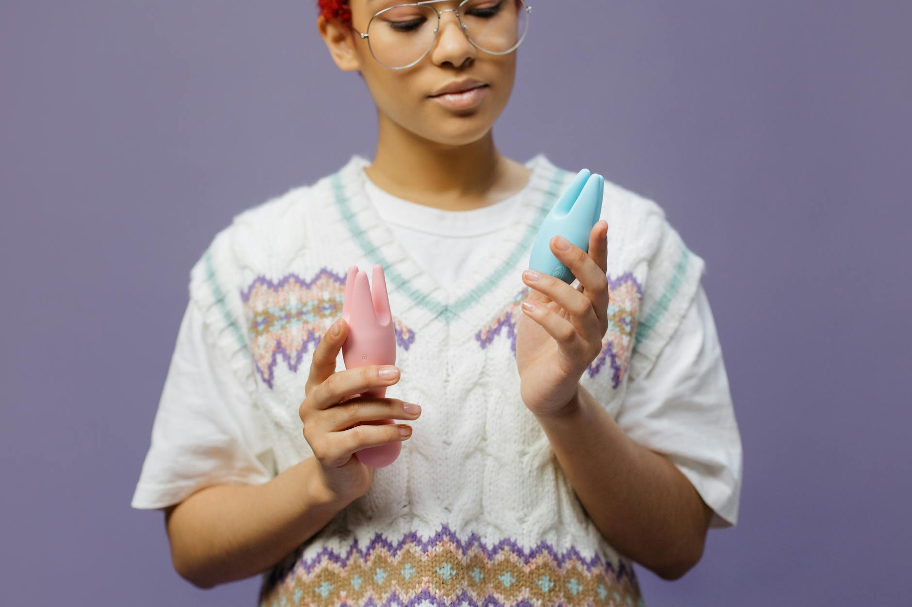 Woman holding blue and pink silicone vibrators, considering which tool to use for arousal training