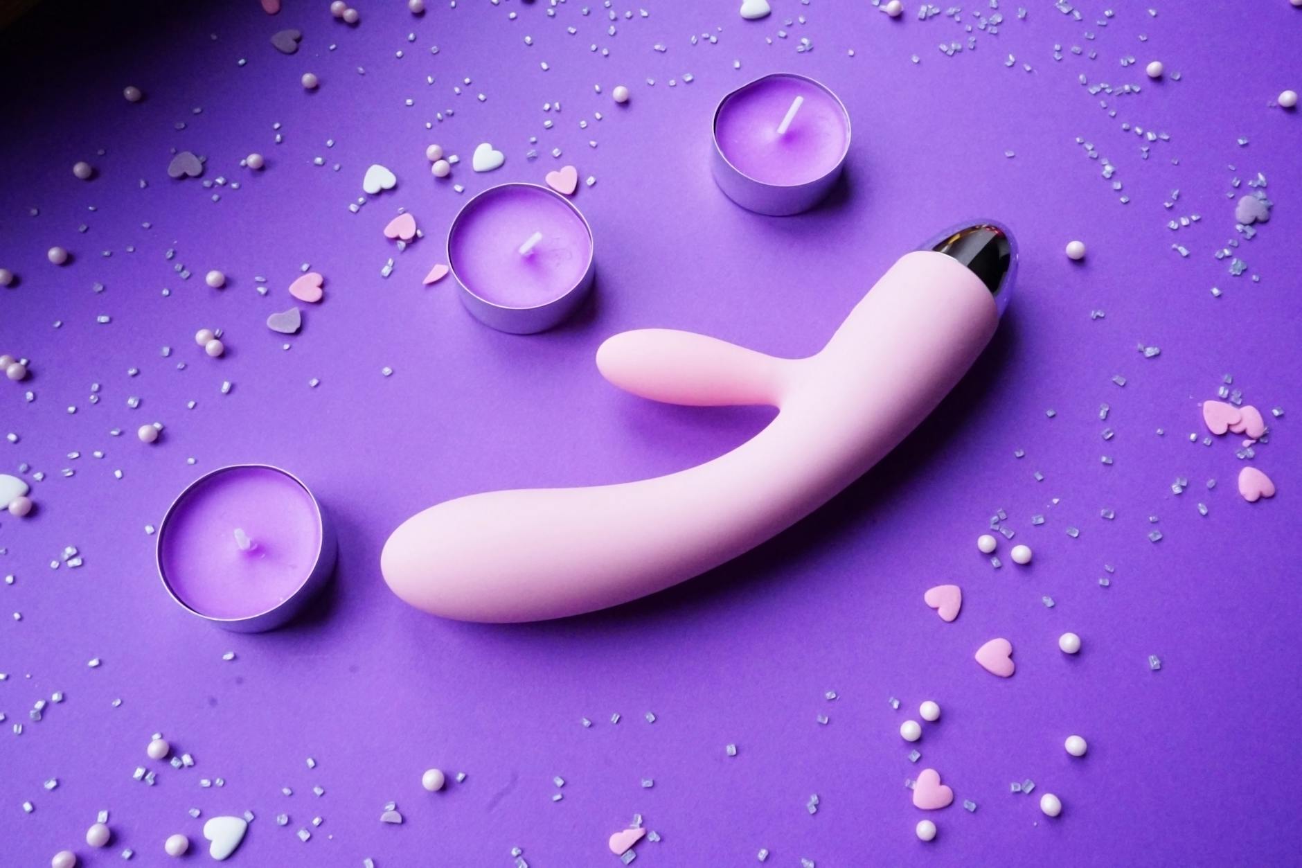 Pink lemon vibrator on purple background with candles and heart confetti, symbolizing intimacy and new romance